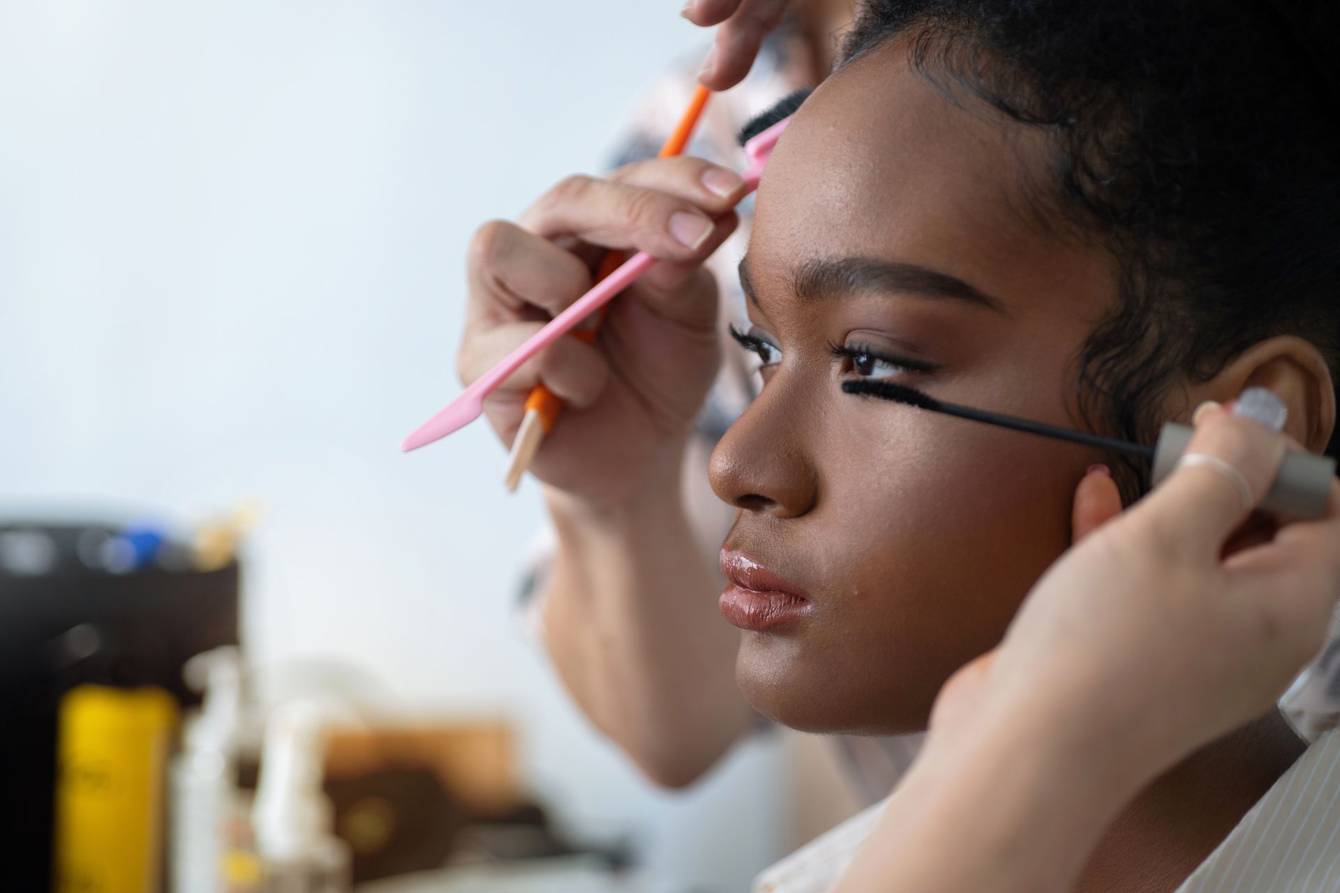 Person receiving a facial mask application. A beautician applies brown mask with a brush, indoors.