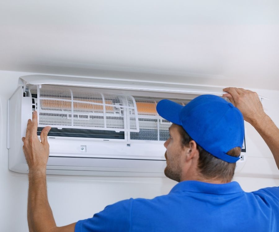 A man in a blue hat is working on an air conditioner.