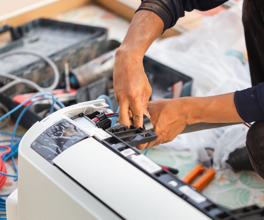 A man is fixing an air conditioner with tools.