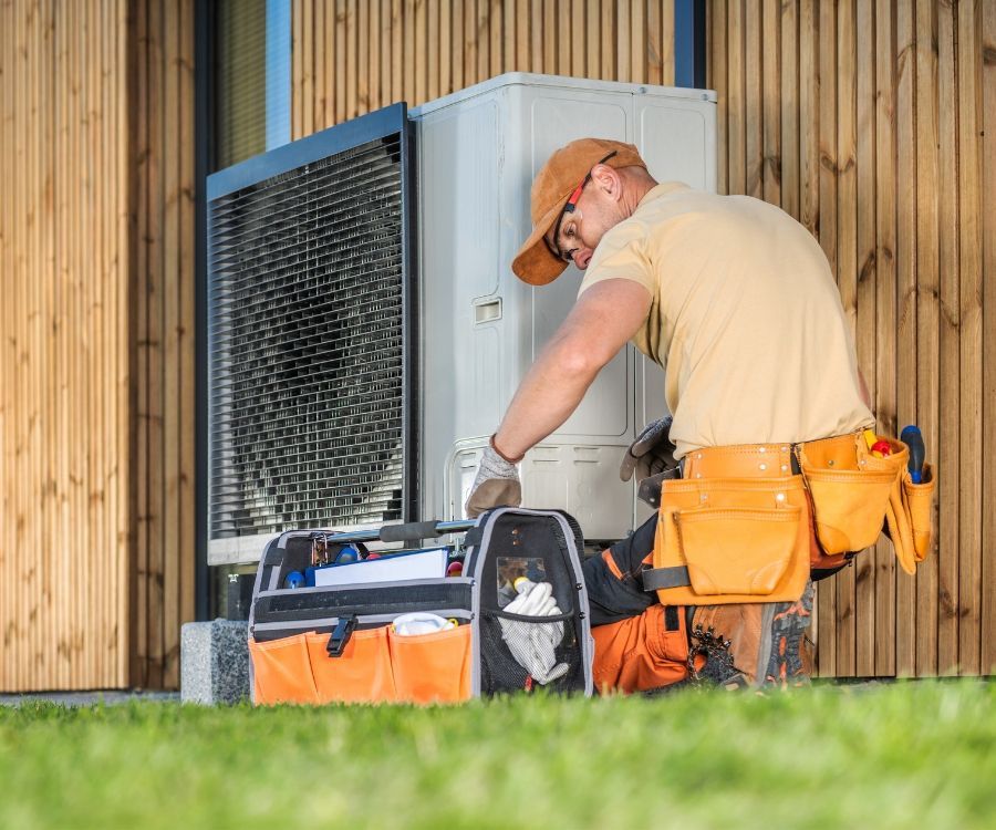 A man is working on a heat pump outside of a house.