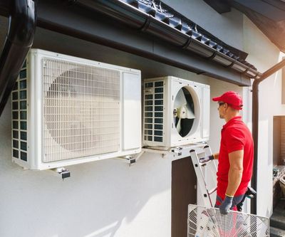 A man is installing air conditioners on the side of a building.