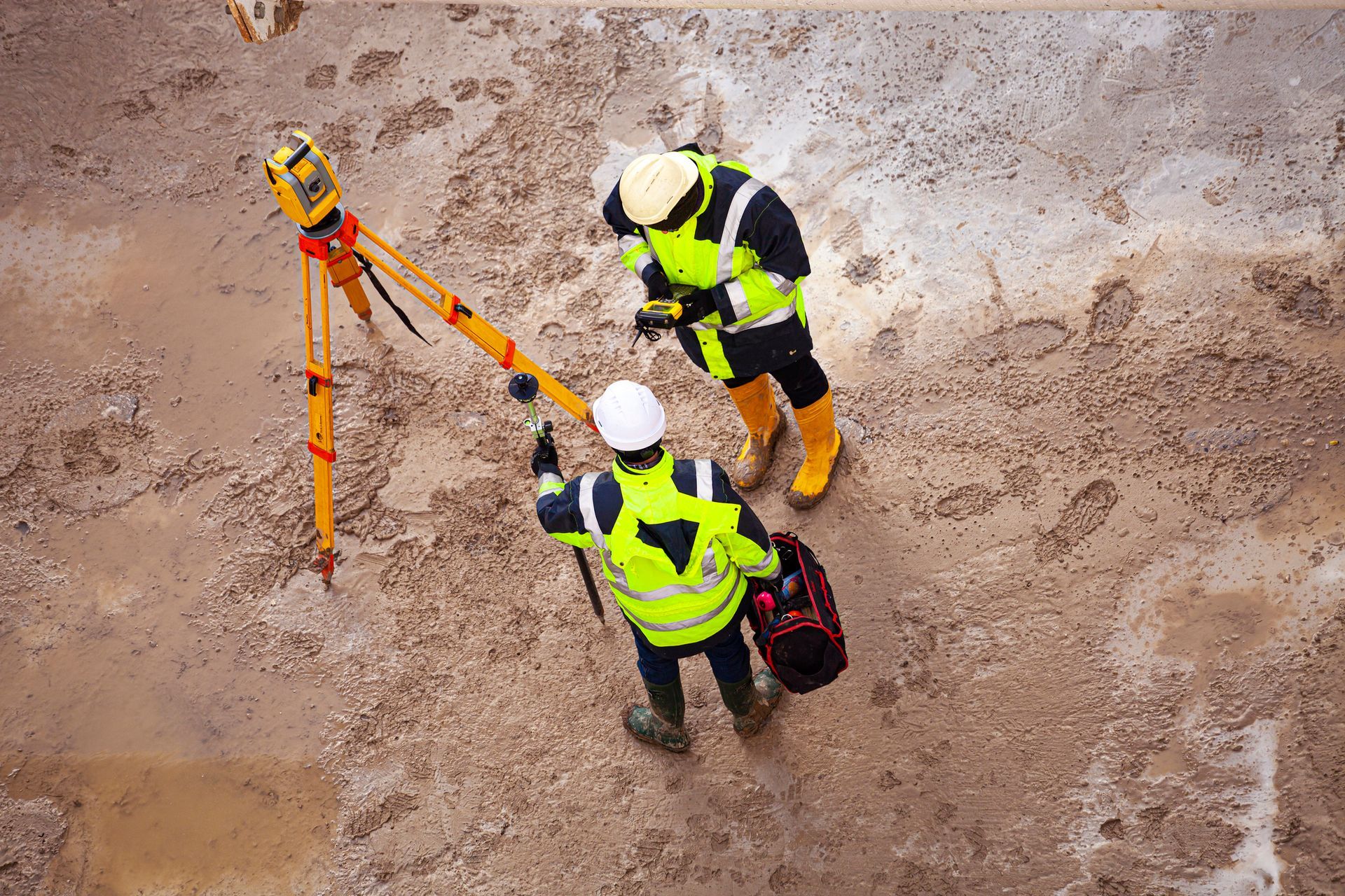 Two construction workers are standing next to each other on a dirt road.