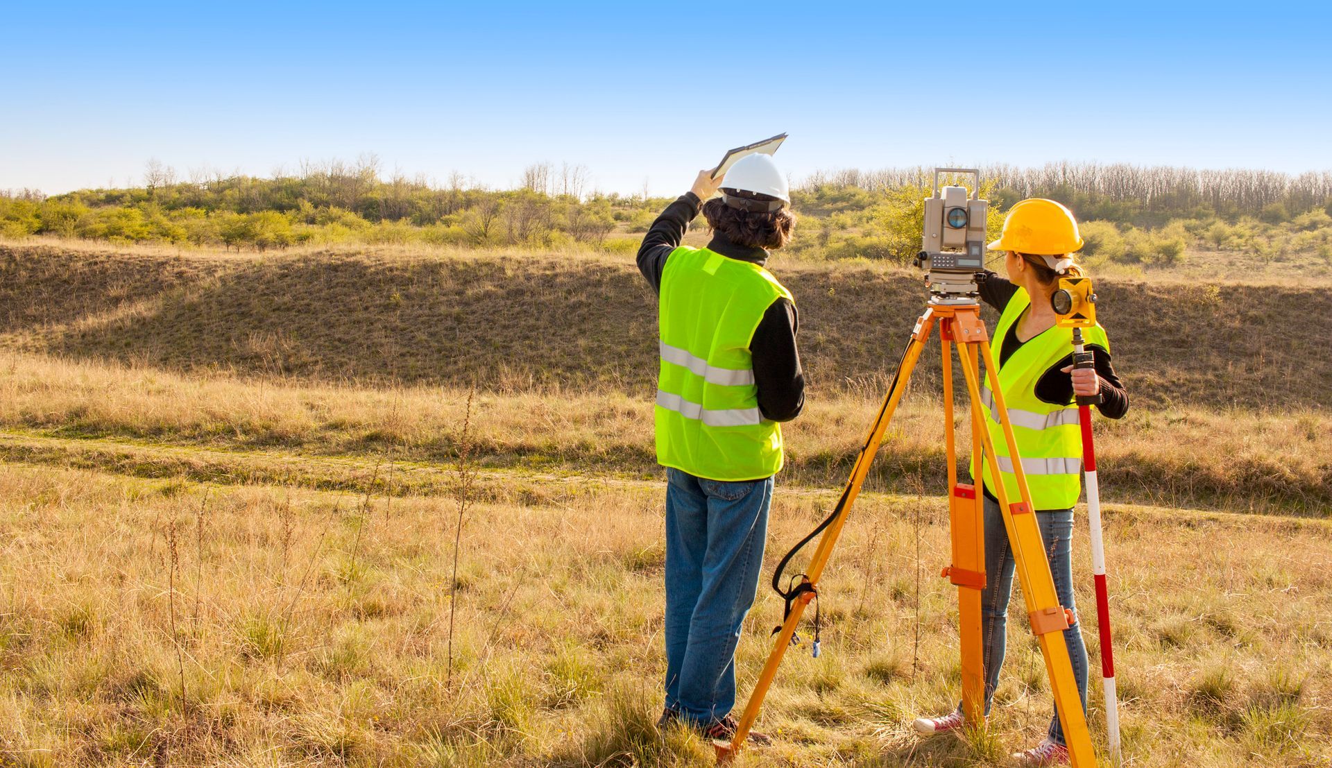 A man and a woman are standing in a field looking at a map.