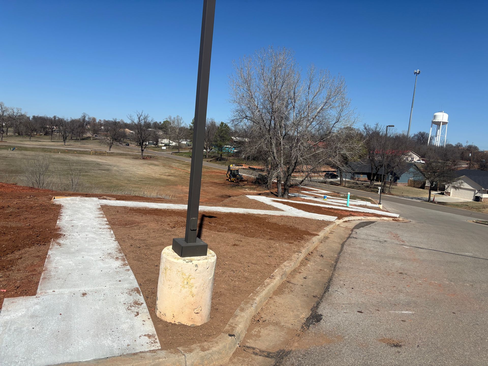 Pathway lined with trees, casting shadows, leading to a building. A person walks in the distance.