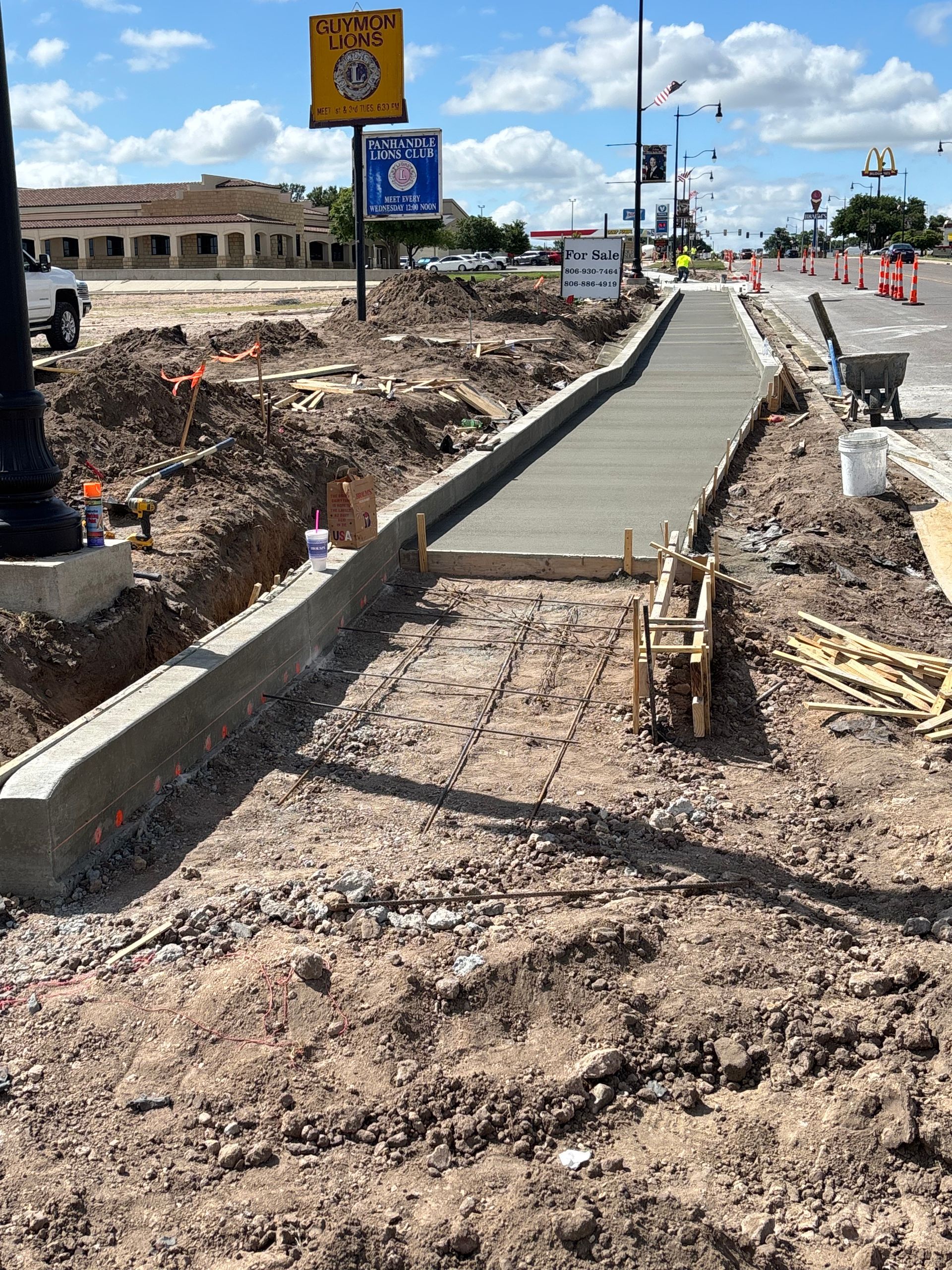 A one-story brick house with a newly poured concrete patio, surrounded by green grass and a cloudy sky.