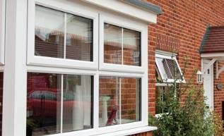 A white bay window on the side of a brick house.