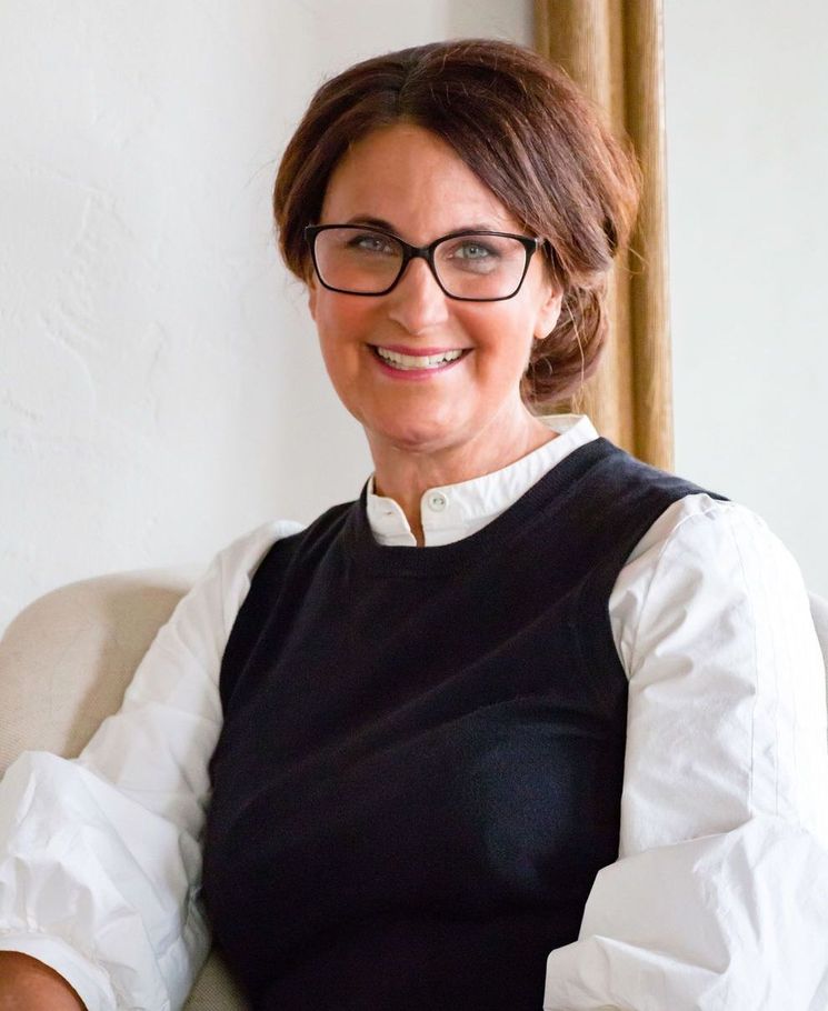 A woman wearing glasses and a black vest is smiling for the camera