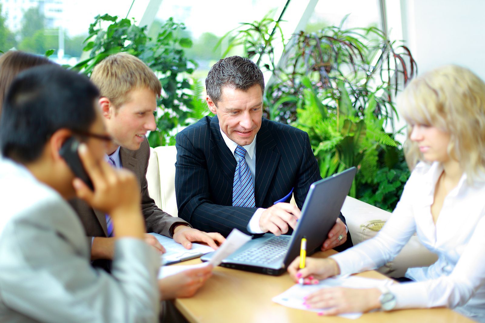 Business team in a web  meeting, focused on a laptop, papers, and taking notes near plants