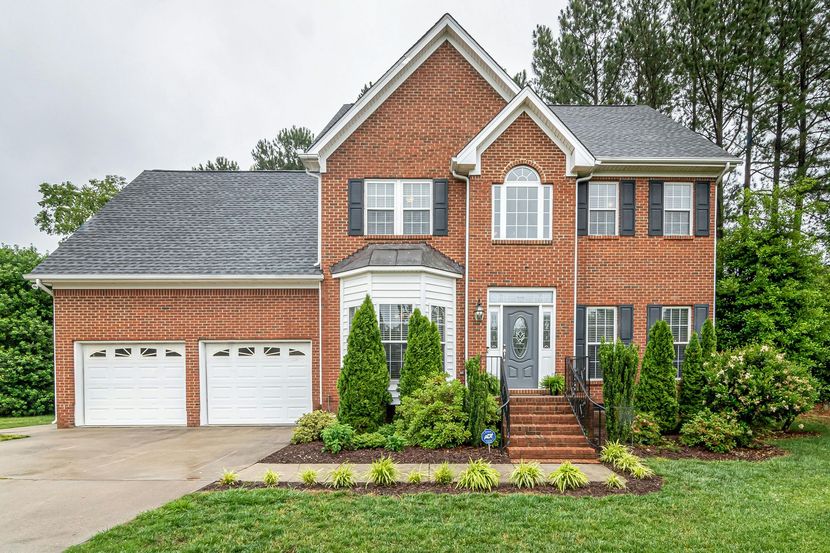 A large brick house with two garage doors and a lush green yard.