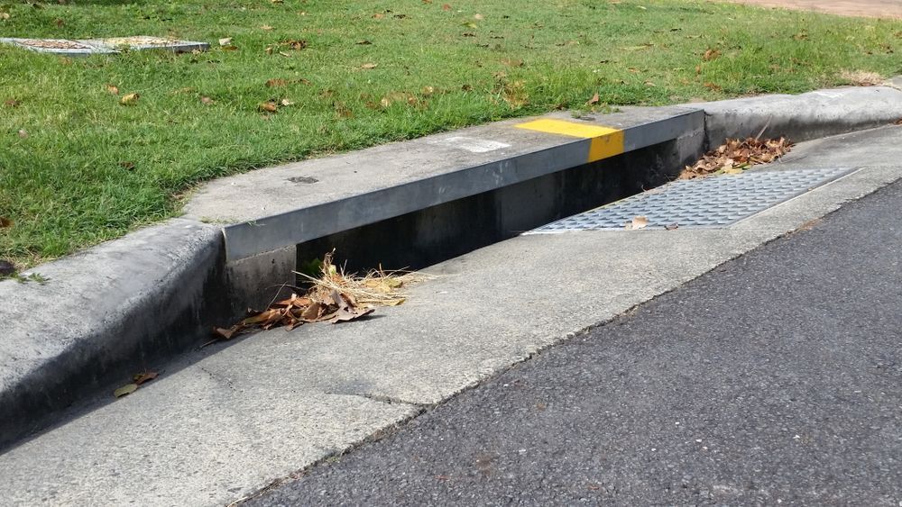 Concrete Curb and Gutter With Grated Drain Along a Paved Road — Sunset Plumbing NT in Moil, NT