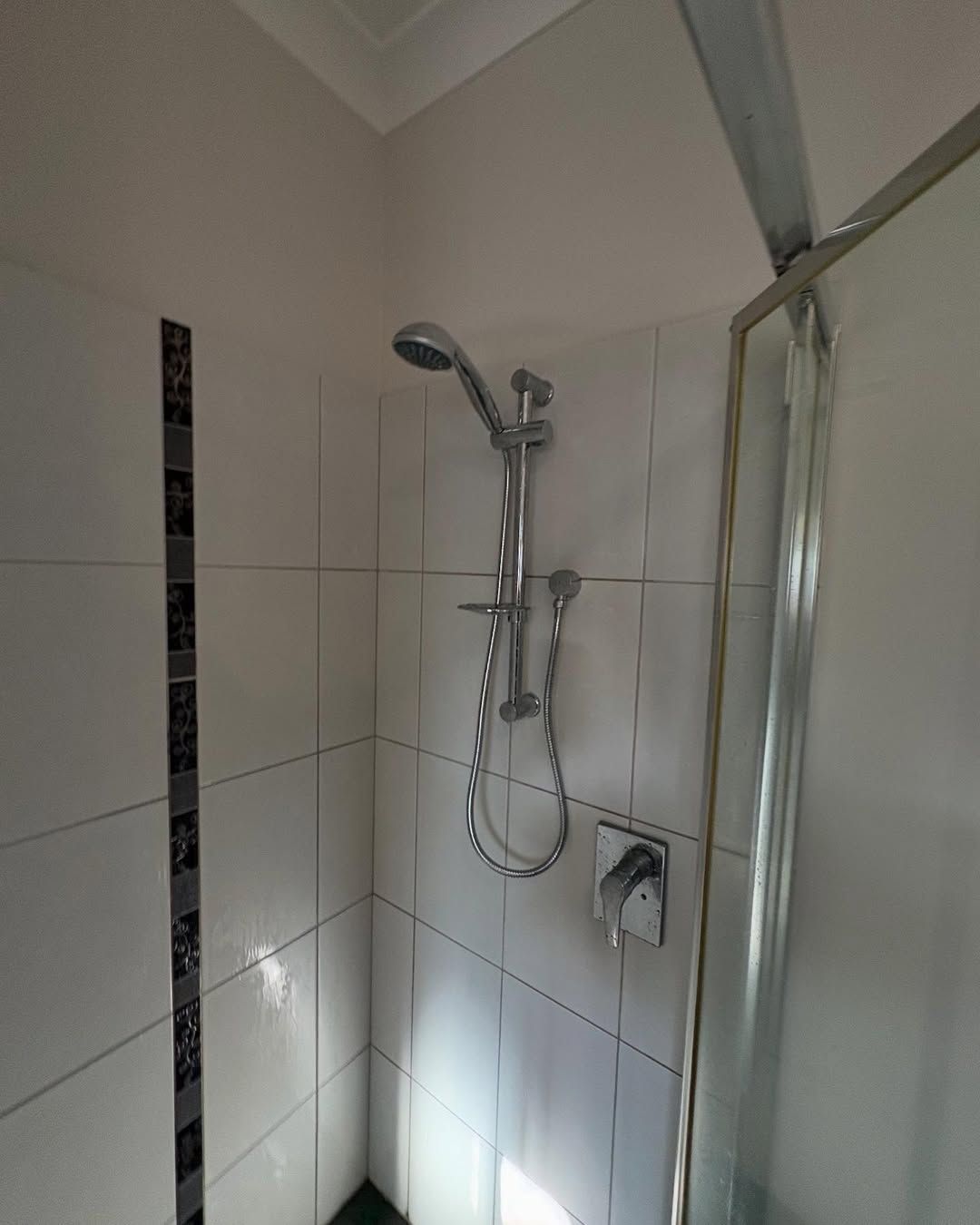 Shower Stall With White Tiled Walls, Silver Showerhead, and a Glass Door — Sunset Plumbing NT in Moil, NT
