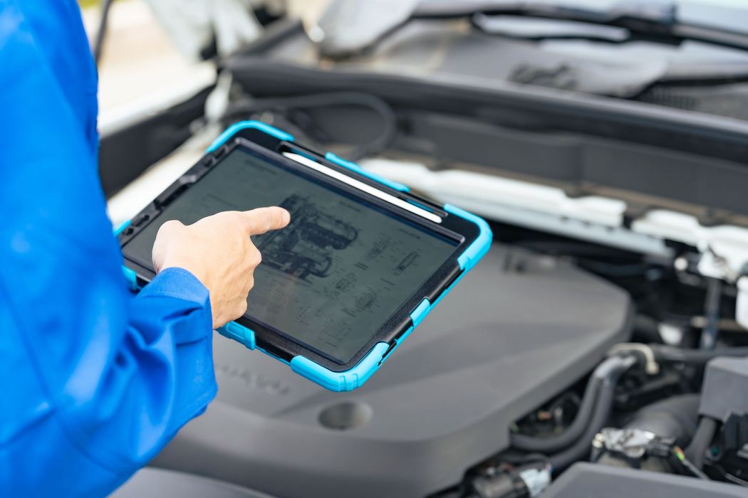 A mechanic is using a tablet to check the engine of a car.