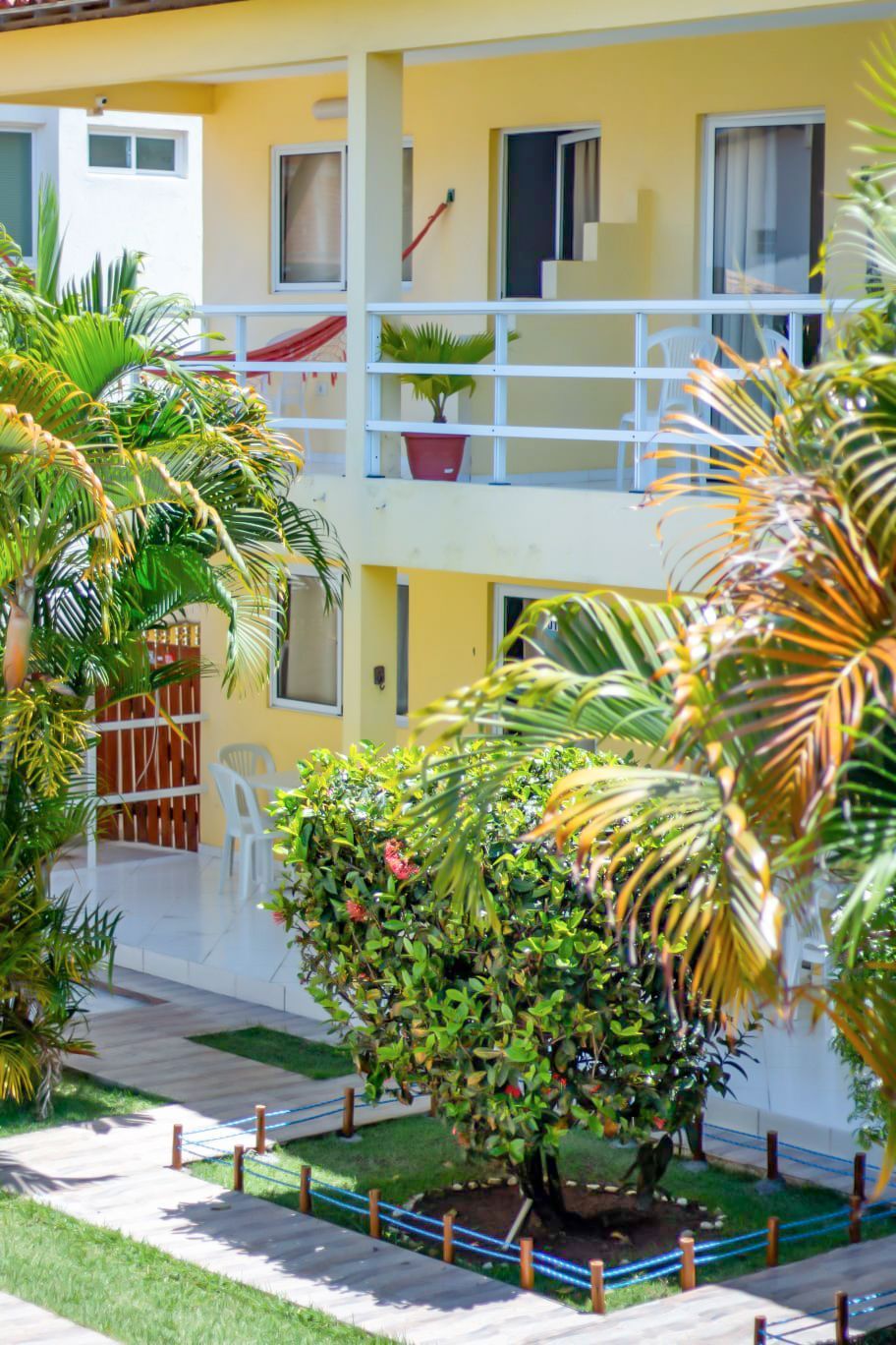 Um grande edifício amarelo com uma varanda e muitas árvores na frente.