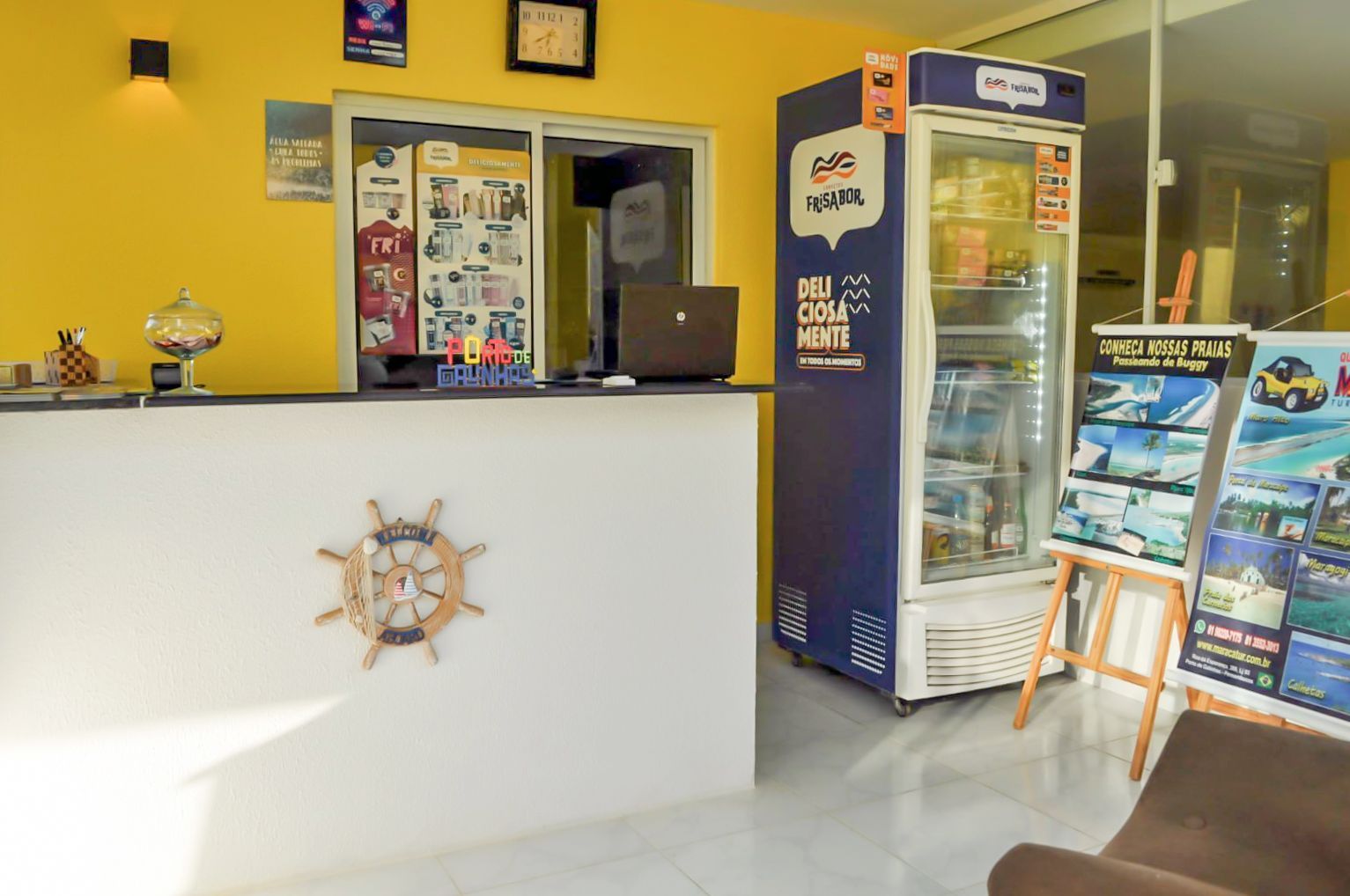 Um lobby de hotel com uma geladeira e um laptop no balcão.