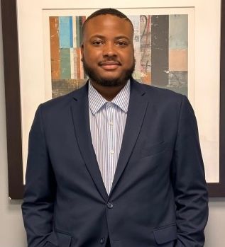 Man in navy suit and striped shirt, smiling in front of abstract art.