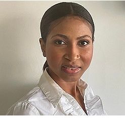 Woman with brown skin, wearing a white collared shirt, looking towards the camera.