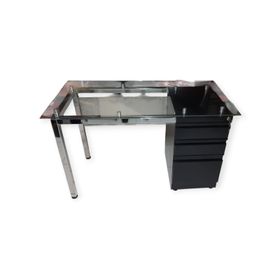 Escritorio con tapa de cristal, patas cromadas y un mueble con cajones de color negro a la derecha.