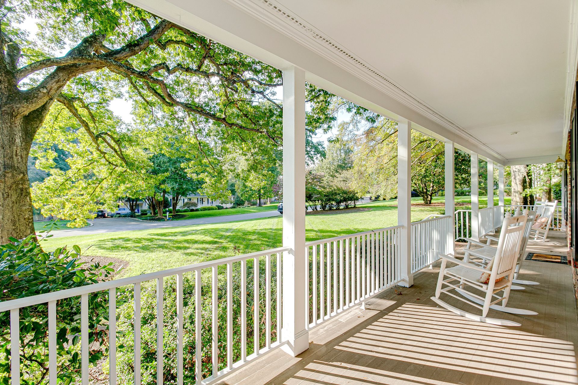 Front porch in the southern countryside on a sunny summer, featuring a tree, warm sunlight, and white rocking chairs.