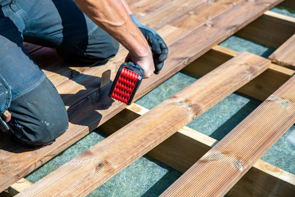 a man is working on a wooden deck with a red tool