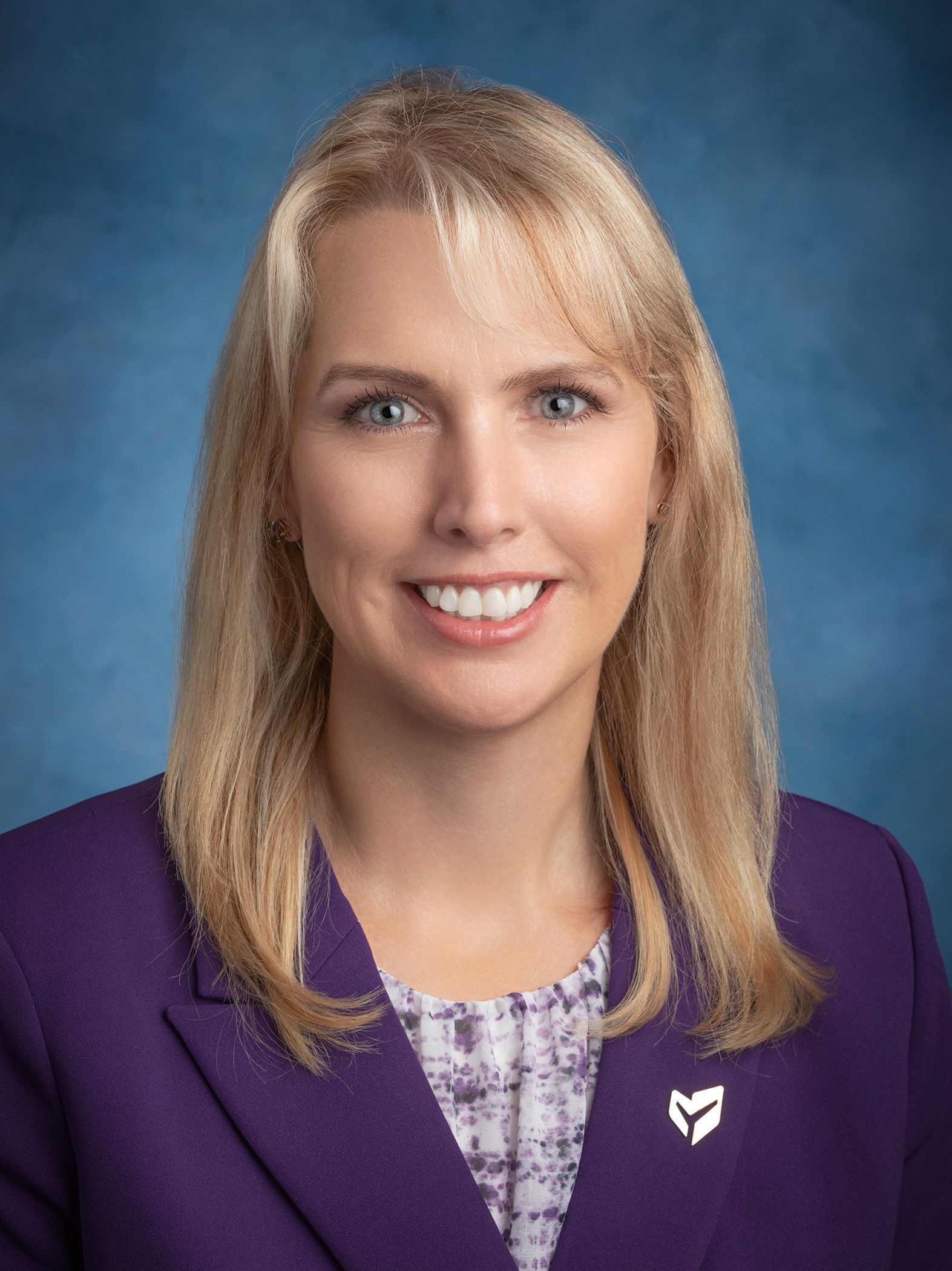A woman in a white jacket is smiling with her hand on her chin.