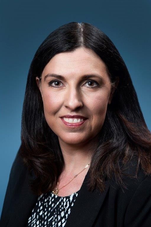 A woman with long dark hair is smiling for the camera in front of a blue background.