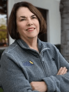 A woman wearing a gray jacket with a yellow bird on it