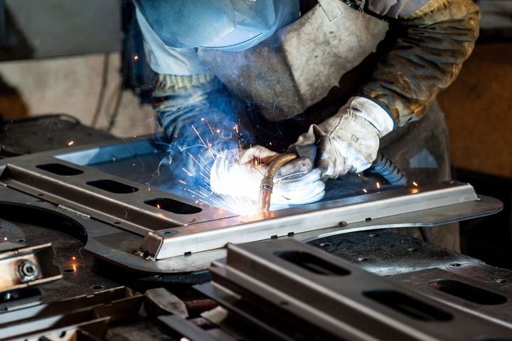 A welder in protective gear uses a torch to join metal pieces on a workbench, creating bright sparks.
