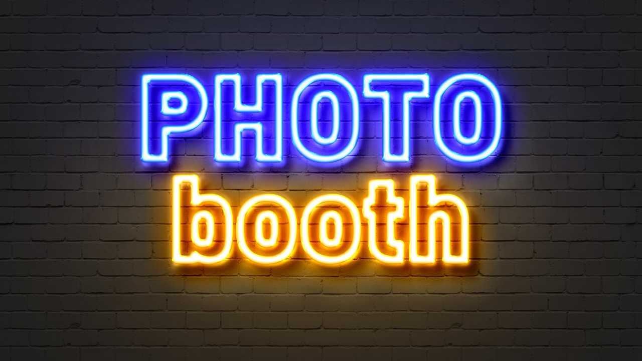 A neon sign that says photo booth on a brick wall.