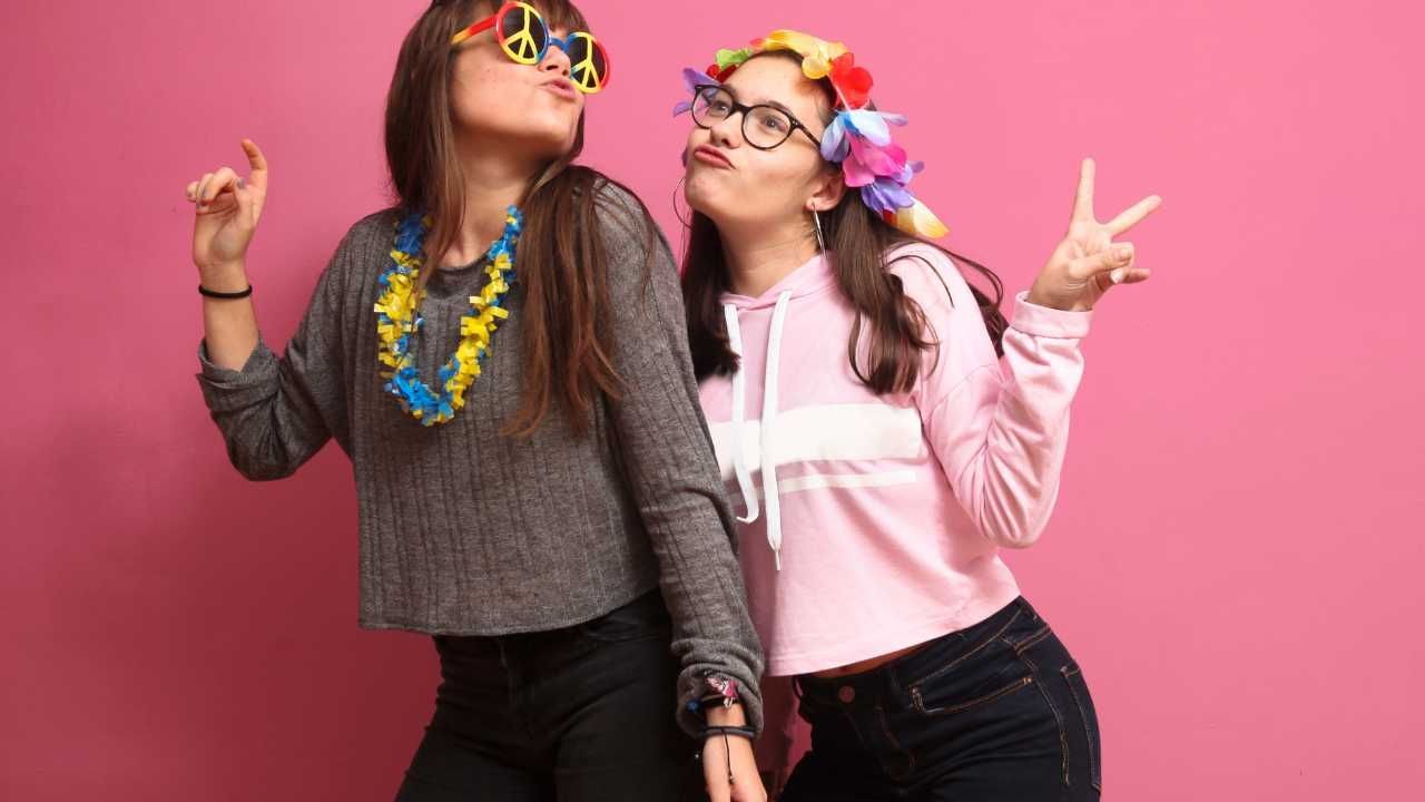 Two young women are standing next to each other on a pink background.