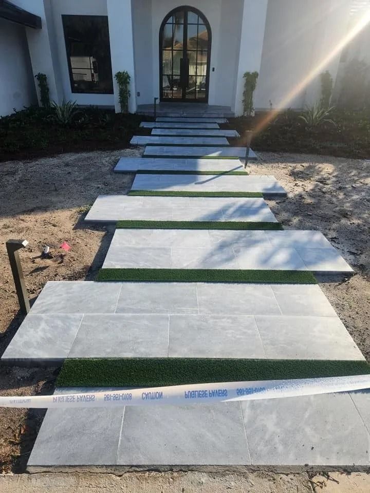 A front entrance path featuring large rectangular gray stone pavers separated by strips of artificial green turf.