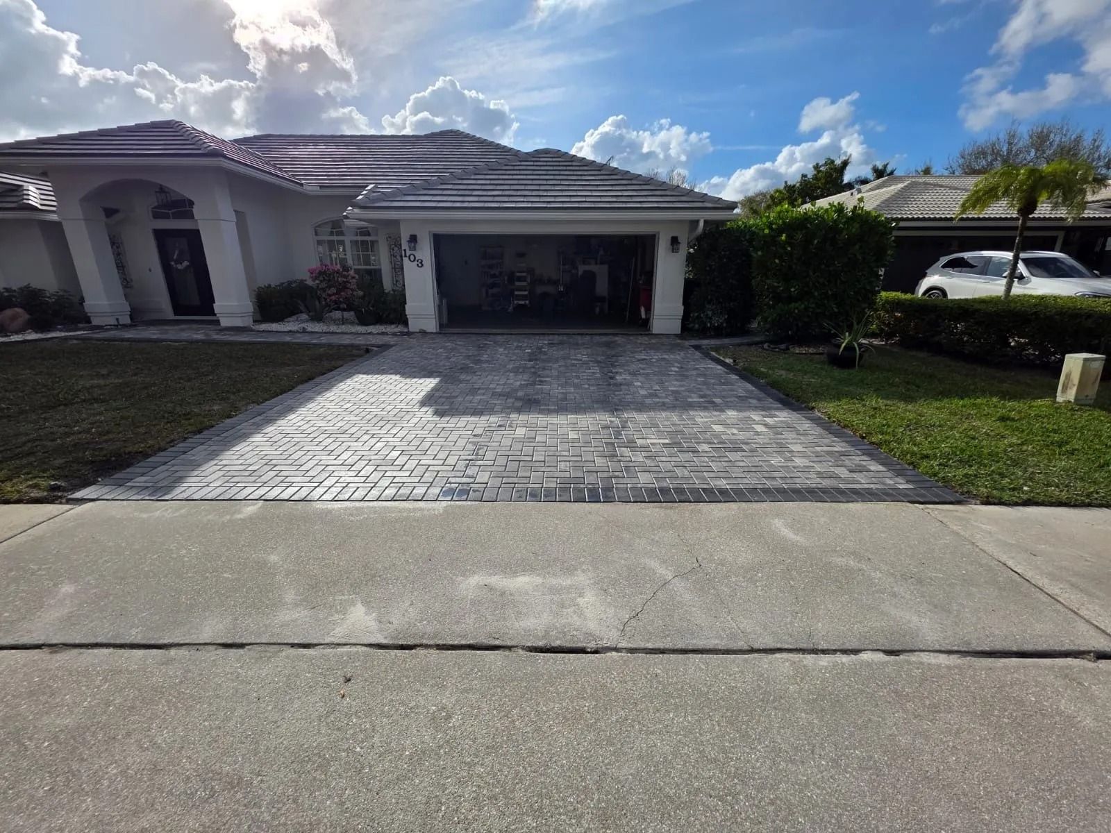 A residential house with a gray tiled roof, white exterior, and a newly installed paver driveway leading to a garage.