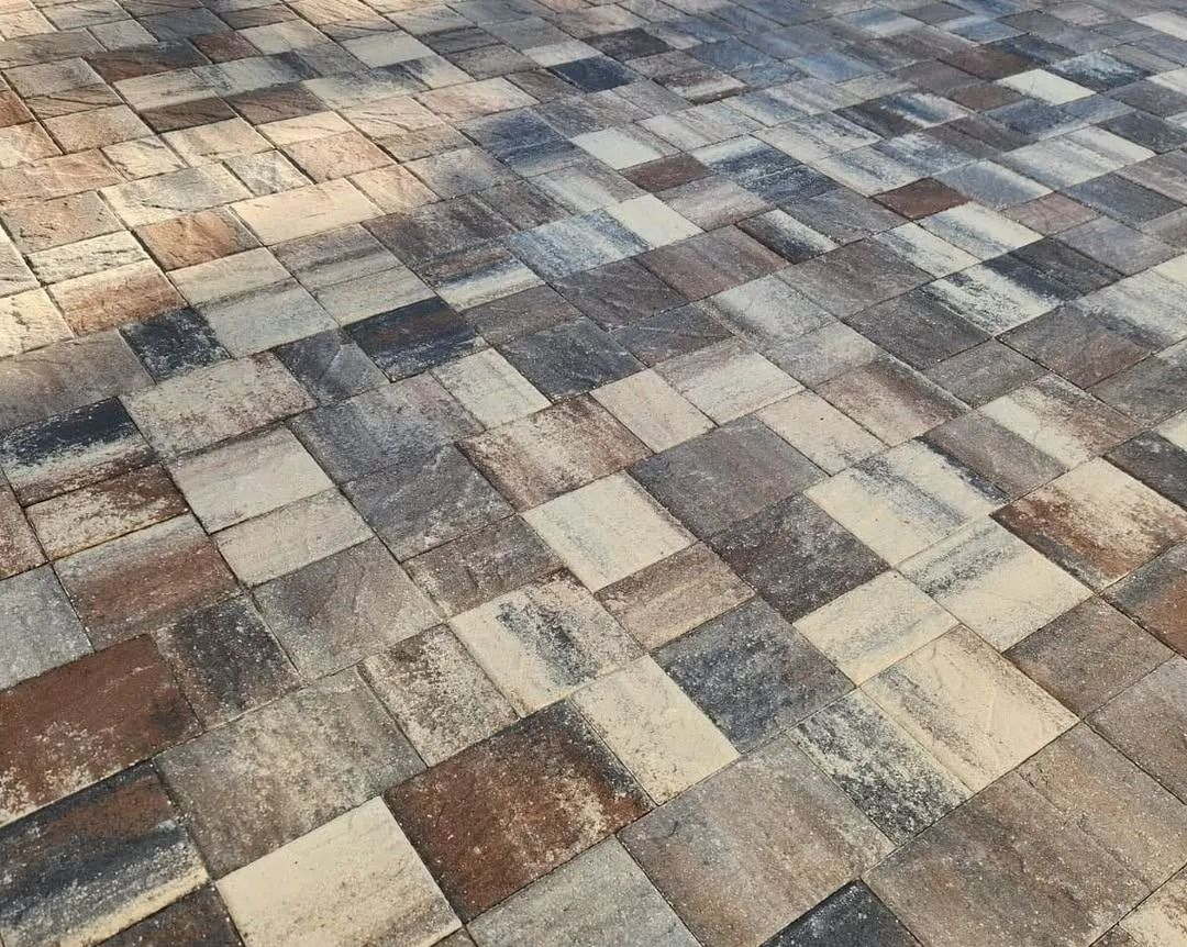 A close-up of a patio surface featuring multi-colored, textured stone pavers in shades of beige, brown, grey, and charcoal.