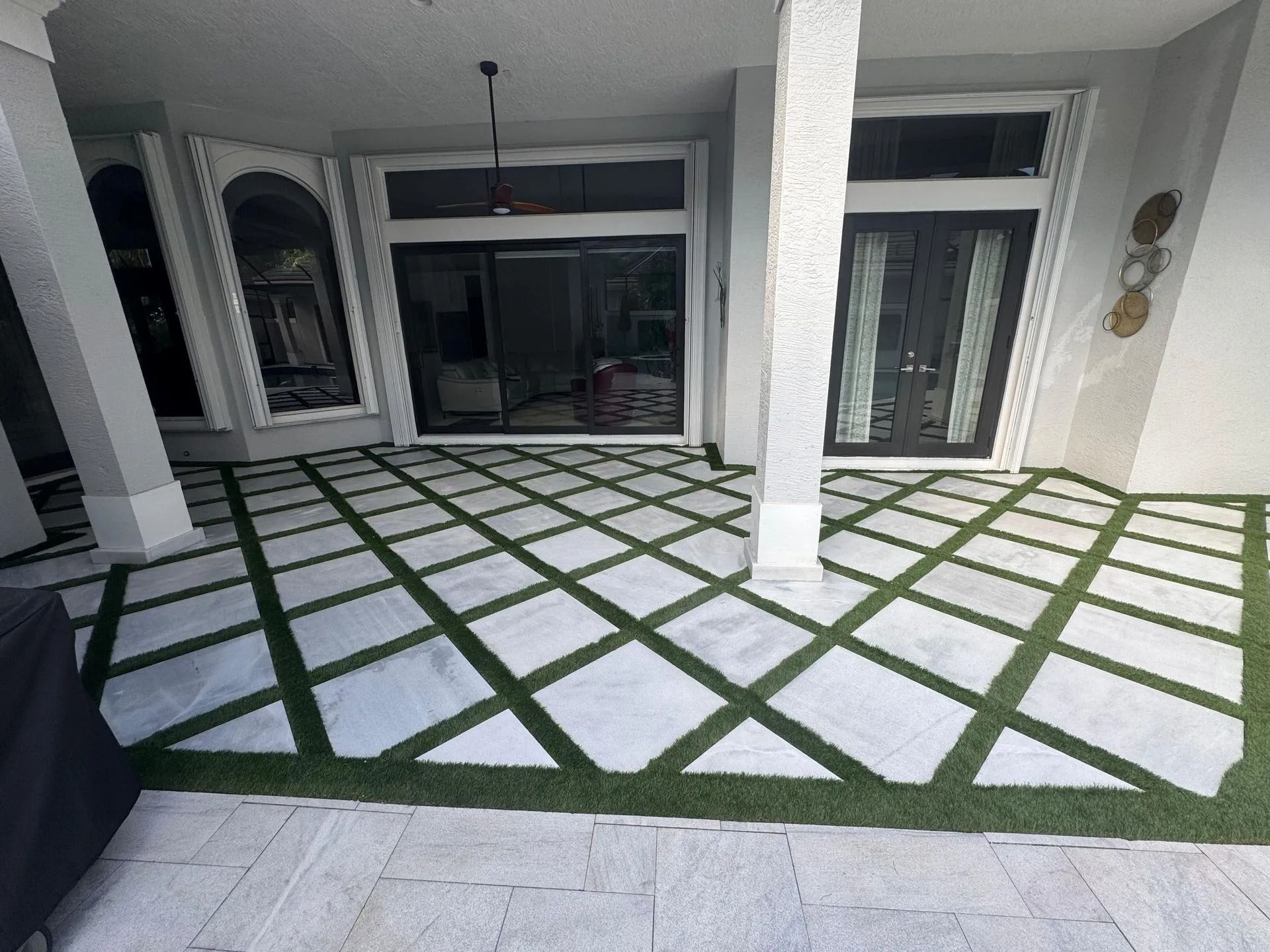 A patio features white diamond-shaped tiles arranged in a grid pattern with green artificial grass between them.