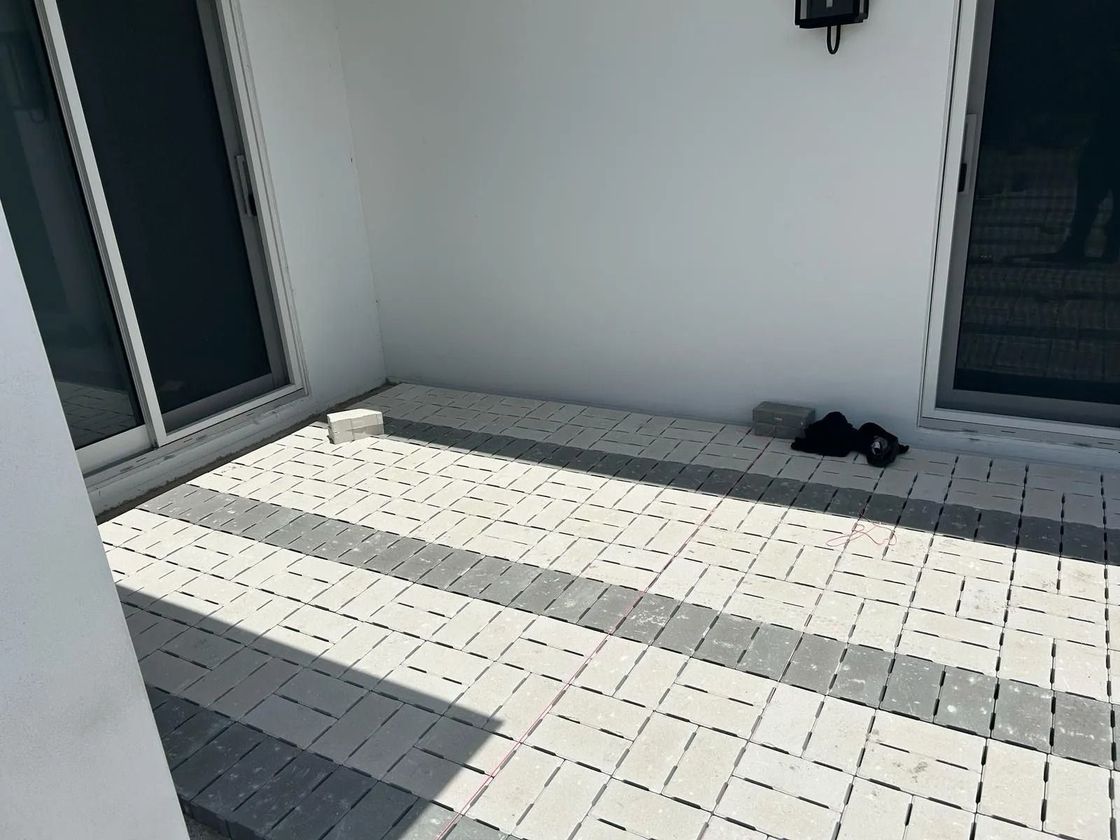 A patio with white and gray rectangular paving stones, flanked by two sliding glass doors on a white-walled house.