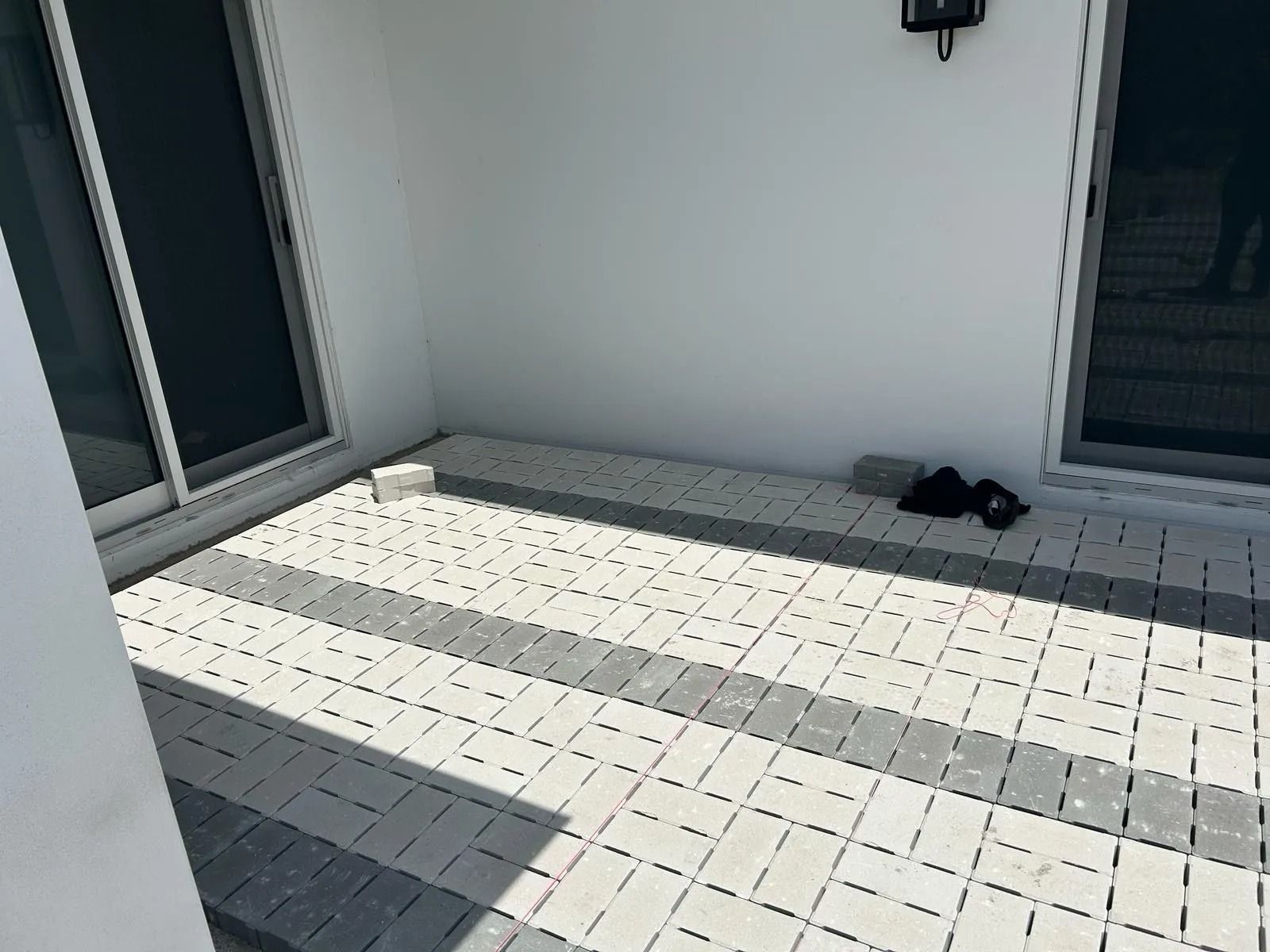 A patio paved with white and gray interlocking bricks, positioned between two sliding glass doors on a white building.