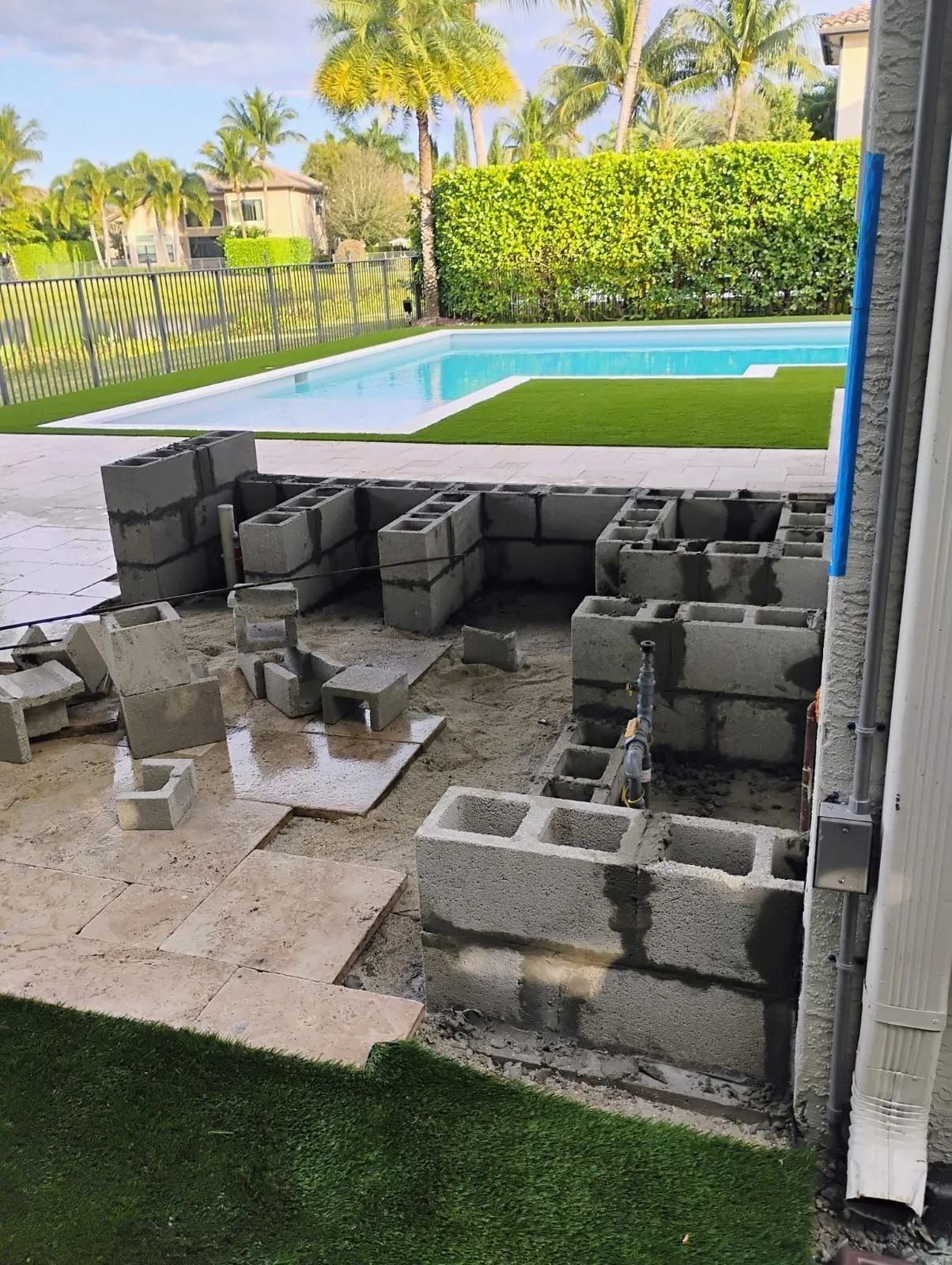 Concrete block construction for an outdoor kitchen in progress on a patio next to a swimming pool.
