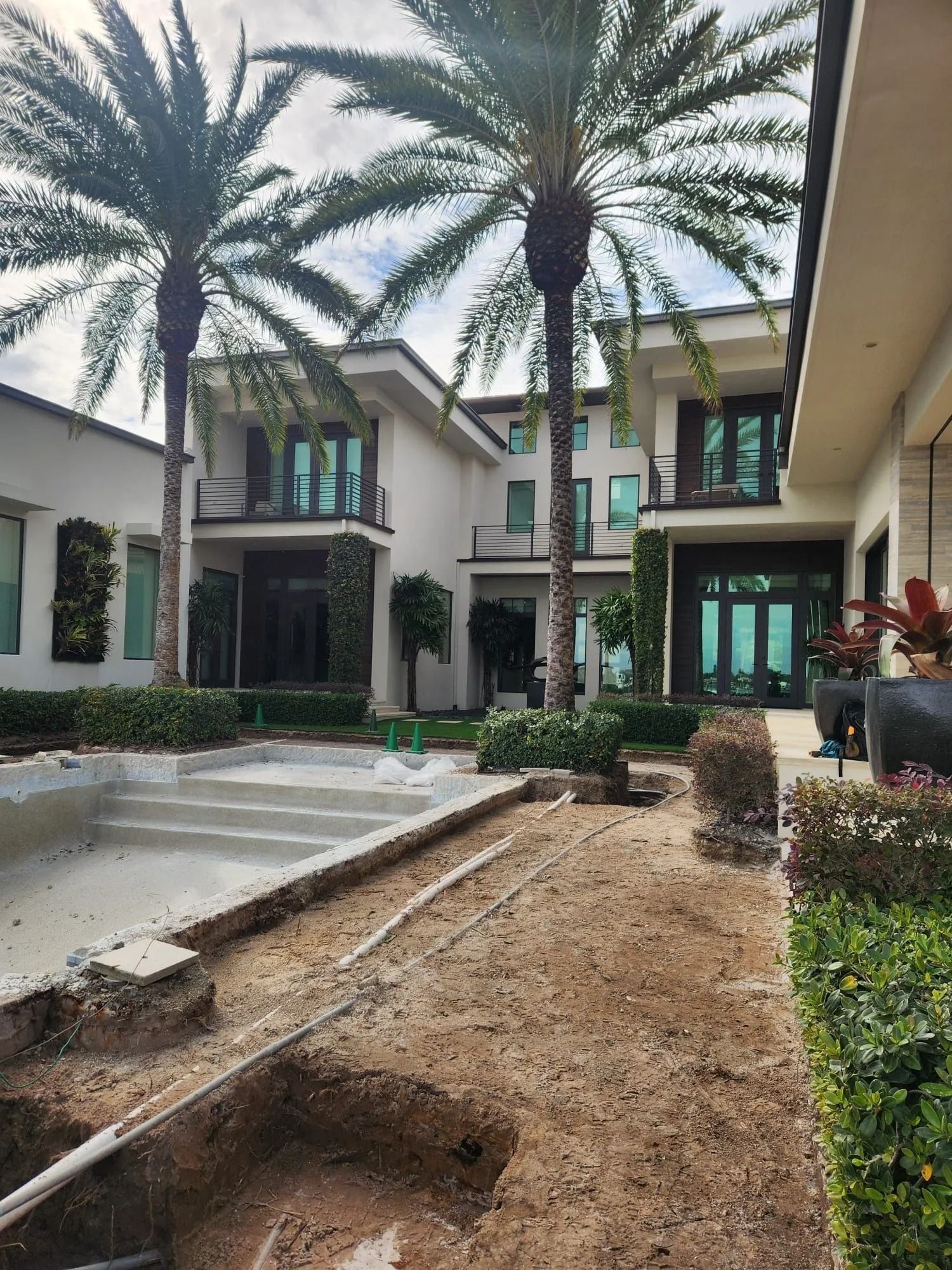 A modern white two-story house with palm trees and a swimming pool under construction in the backyard.
