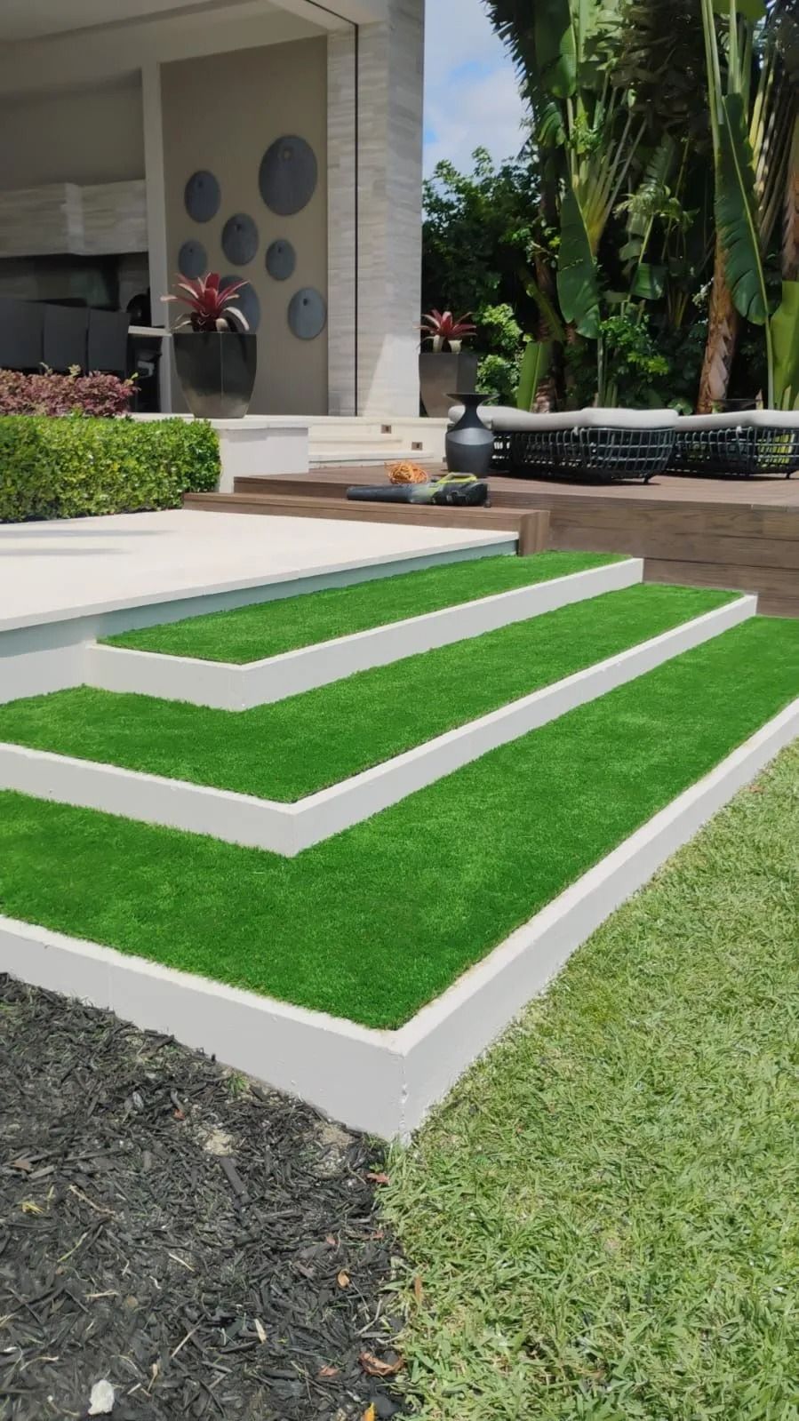 Modern patio steps covered in artificial grass, bordered by white stone, next to a black gravel garden bed and lawn.