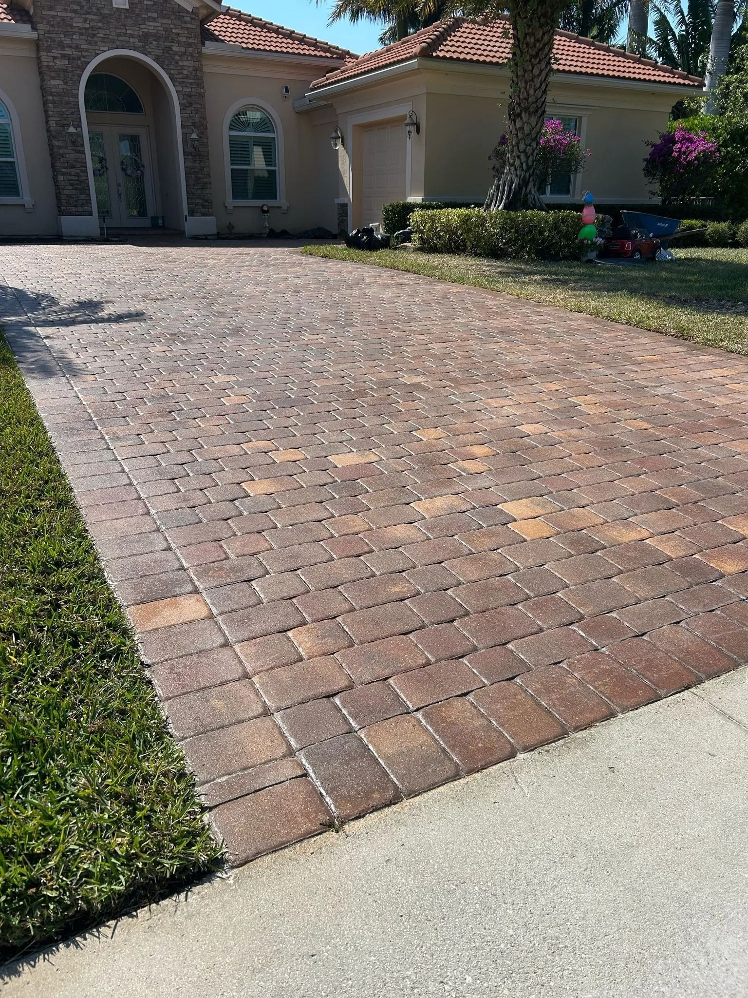 A brick-paved driveway leads to the entrance of a house with stone accents and a terracotta roof.