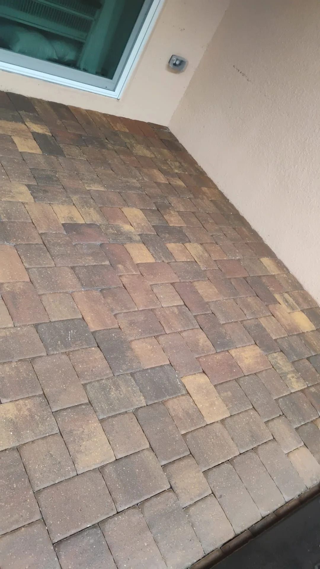 A paved patio area featuring multi-colored rectangular bricks in a herringbone pattern next to an exterior building wall.