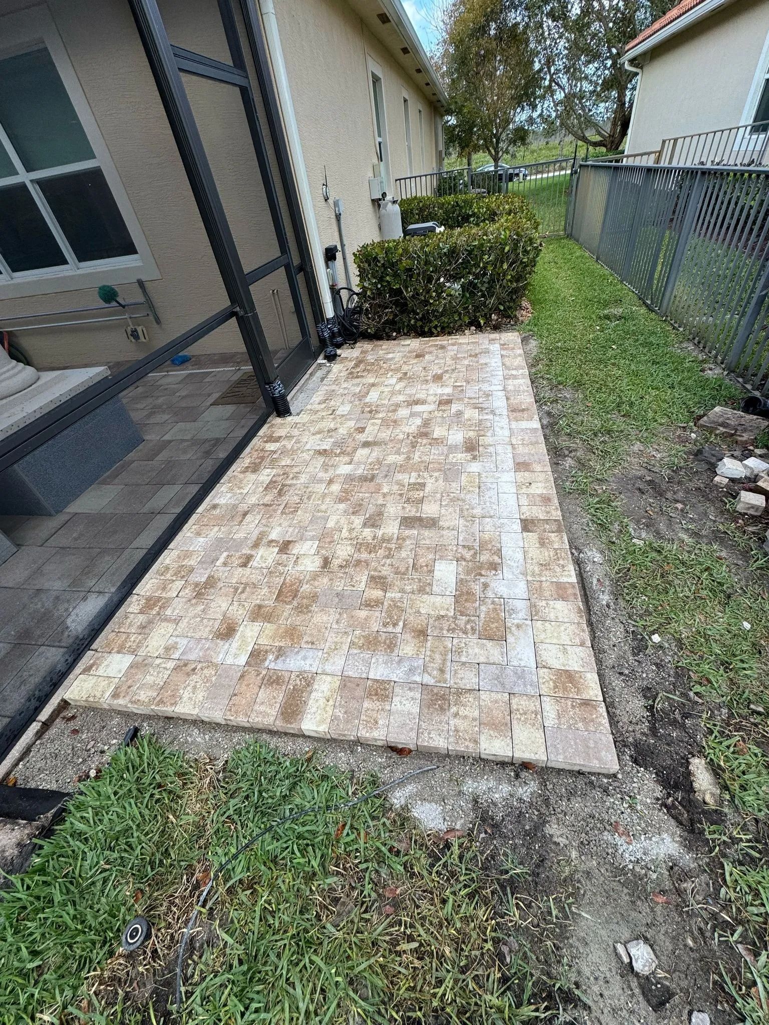 A rectangular patio made of light-colored, patterned stone pavers located next to a house with a screen enclosure.