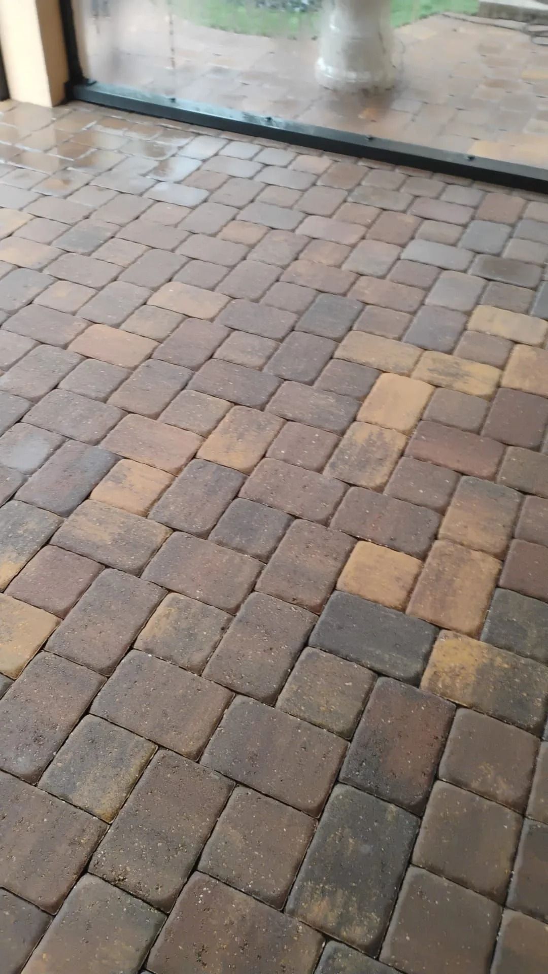 Close-up of a paved patio floor made of rectangular bricks in varying shades of brown, tan, and gray.