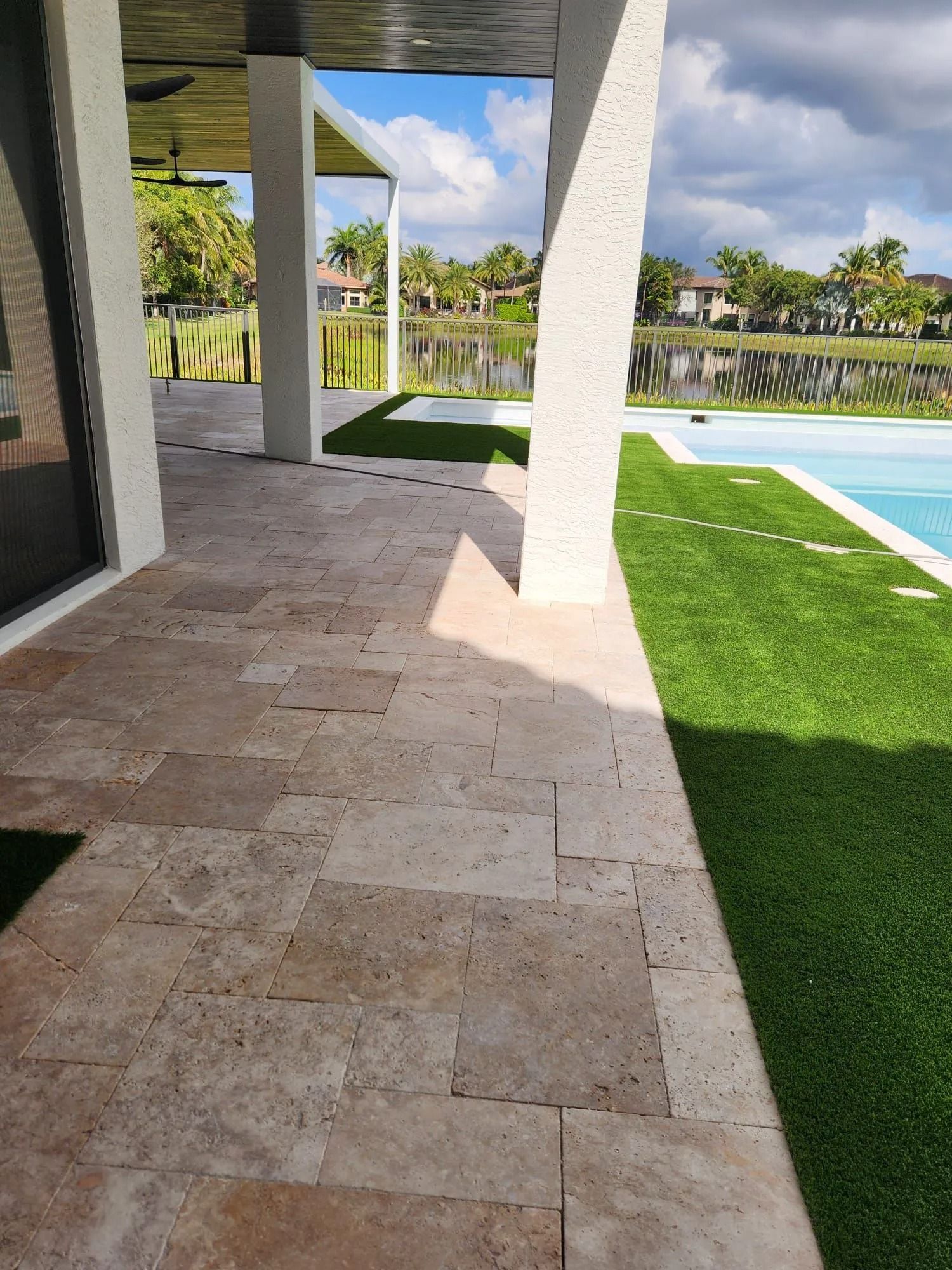 Tan travertine patio tiles under a covered lanai, with a green lawn and swimming pool visible in the background.