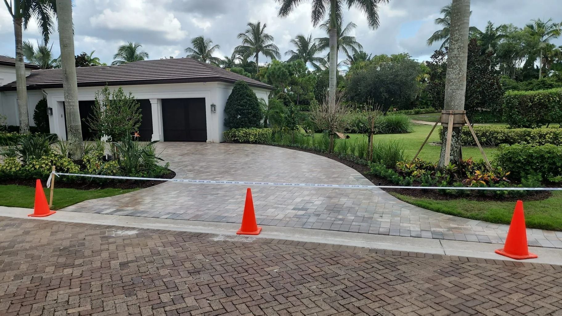 A paved driveway leading to a house entrance with three orange traffic cones positioned in the foreground.
