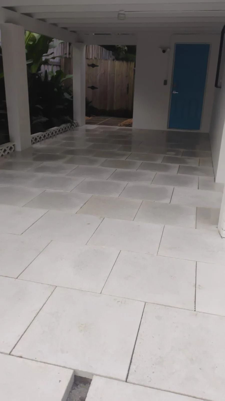 A covered patio featuring light-colored, square stone floor tiles and a bright blue door in the background.