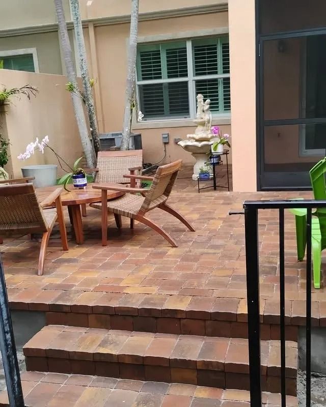 A brick-paved patio with steps, outdoor furniture, and a decorative stone fountain in a courtyard setting.