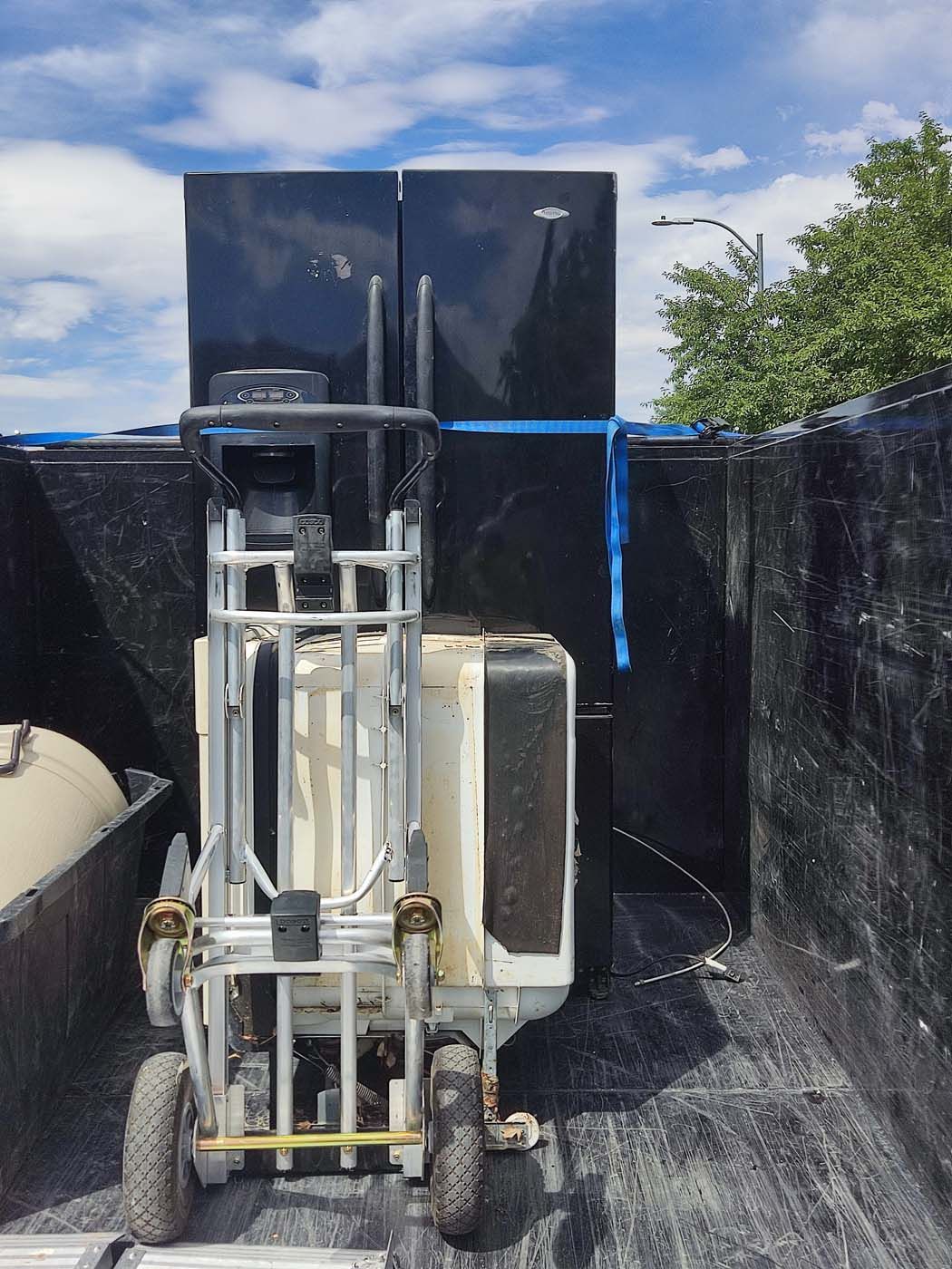 A forklift is carrying a refrigerator in a truck bed.