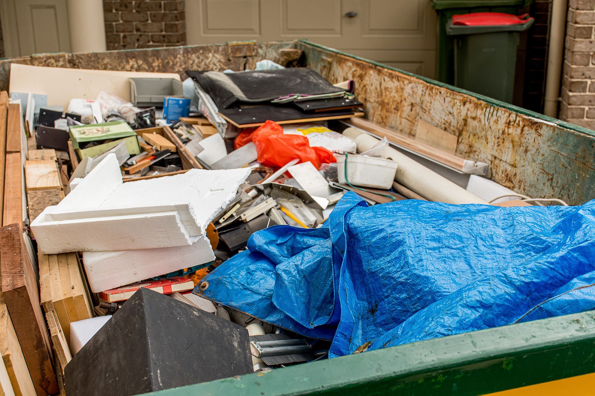 A dumpster filled with lots of trash and a blue tarp.