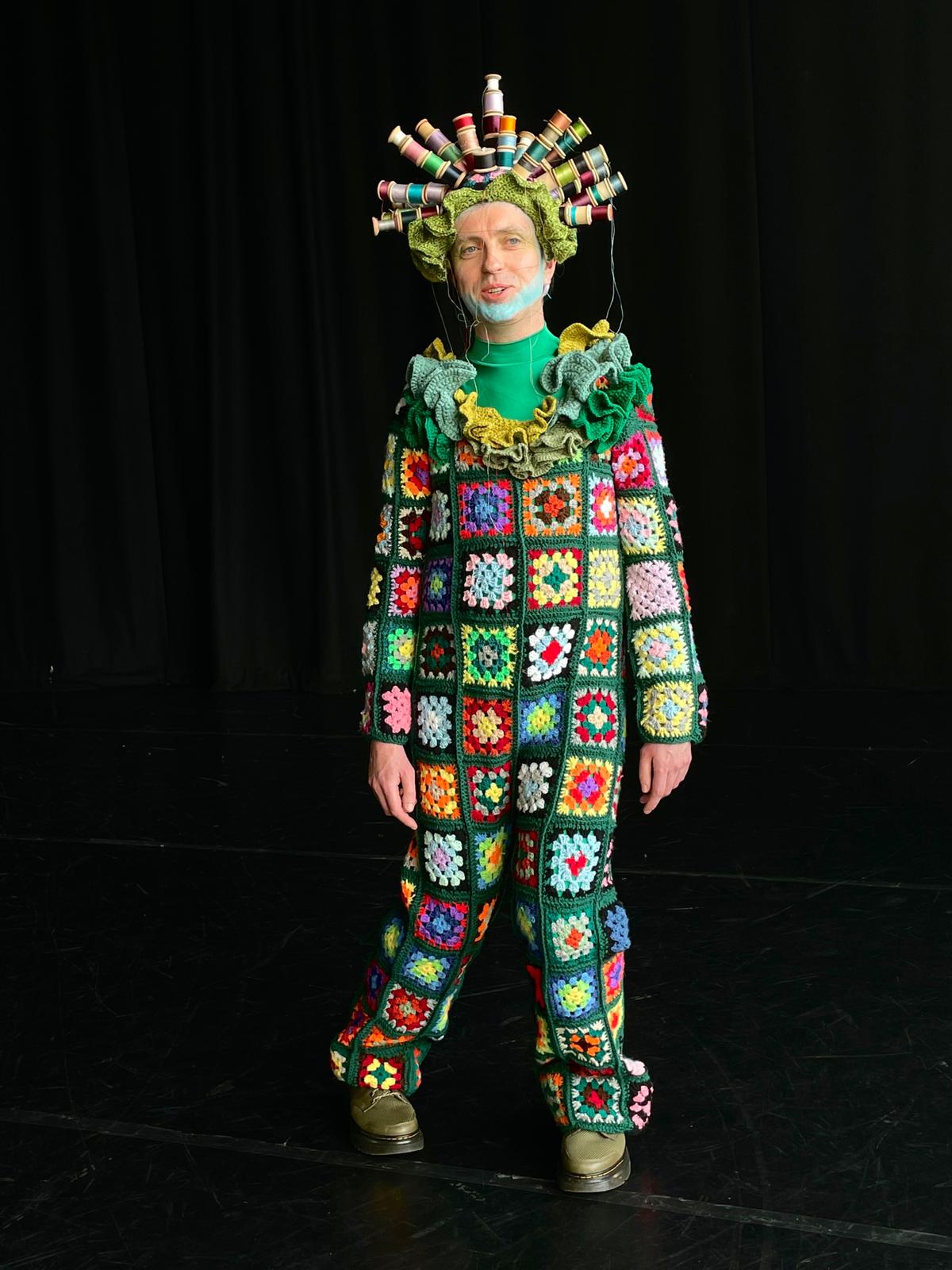 a man in a colorful crocheted outfit is standing on a stage .
