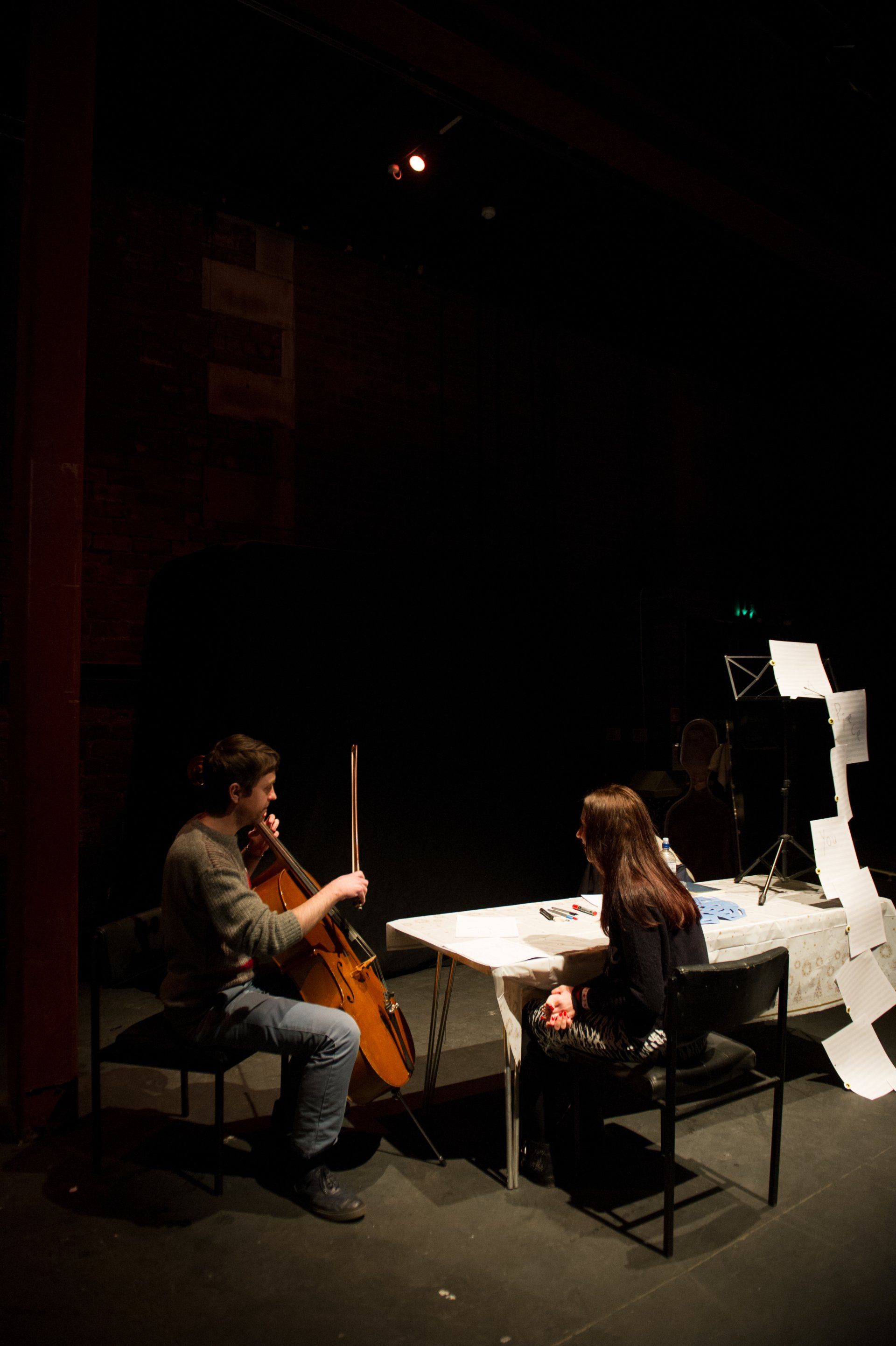 a man is playing a cello on a stage while a woman sits at a table .